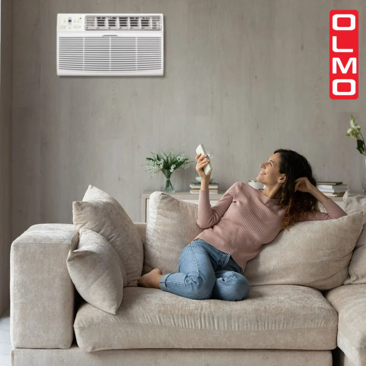 Woman sitting on a couch using a smartphone with an air conditioner above her.